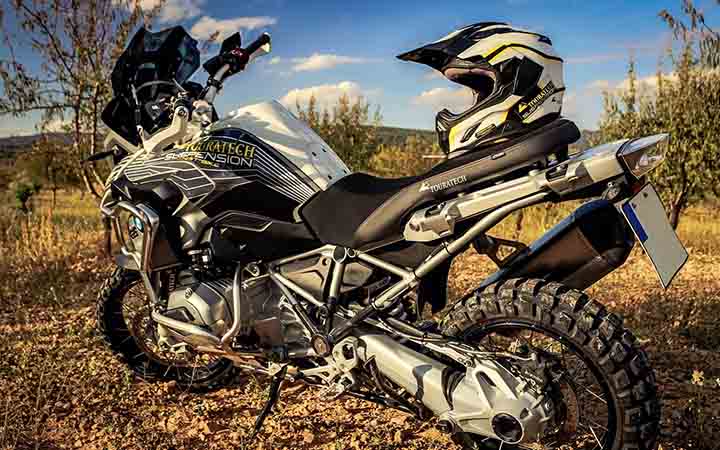 Ein weiss-schwarzes Enduro-Motorrad steht in einem Wladstueck; auf dem Motorrad liegt der Helm 
