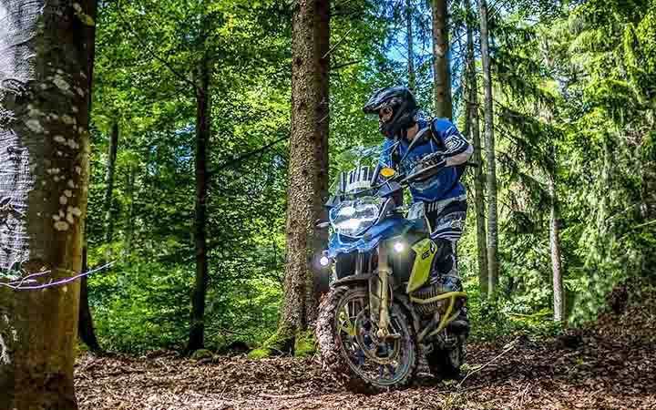 Ein Motorradfahrer fahrt mit seiner Enduro durch einen Parkour zwischen Baeumen in einem Waldstueck hindurch