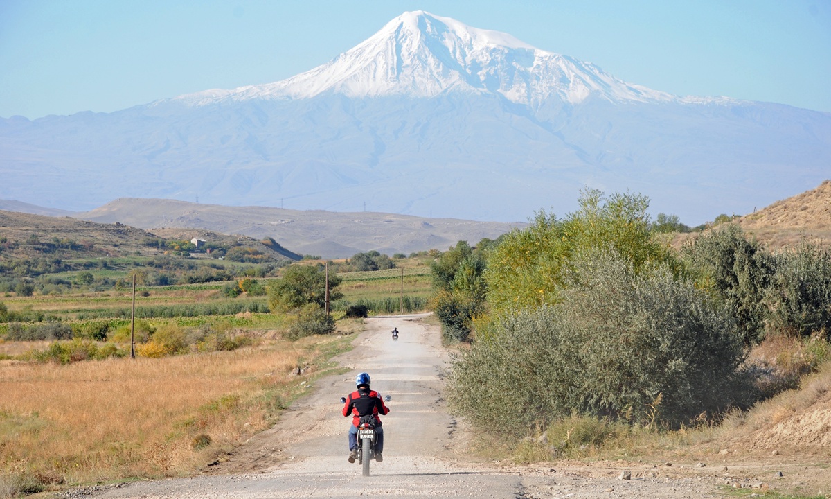 Ein Motorrad faehrt einen Feldweg in Armenien entlang der gerade auf einen hohen schneebedeckten Berg zufuehrt