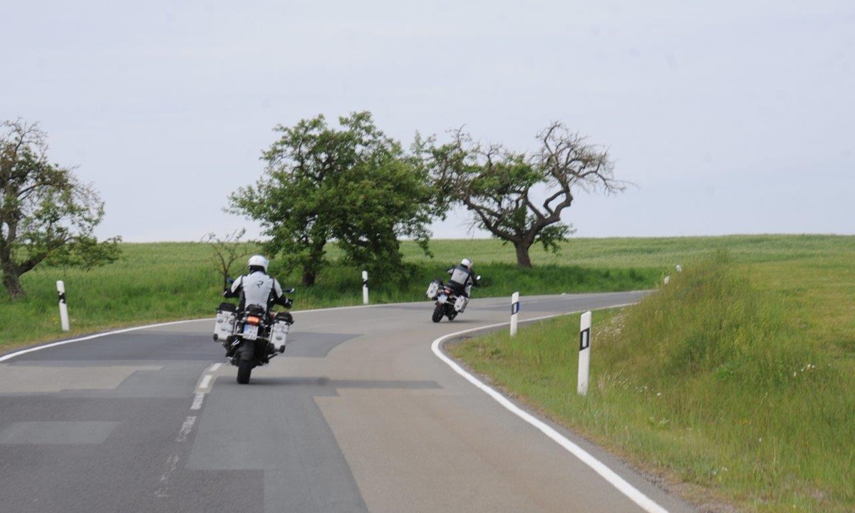 Zwei Motorradfahrer durchfahren die Kurve einer Landstrasse mit Getreidefeldern darum