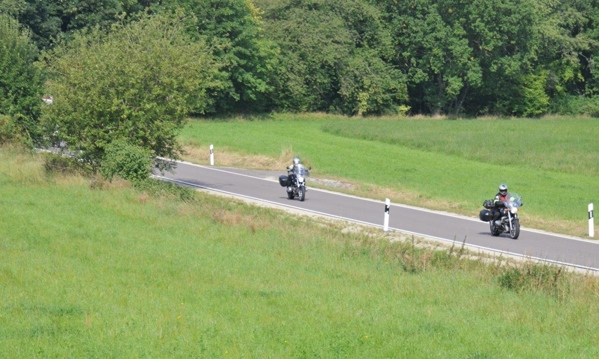 zwei Motorraeder fahren auf einer Landstrasse ueber gruene Wiesen
