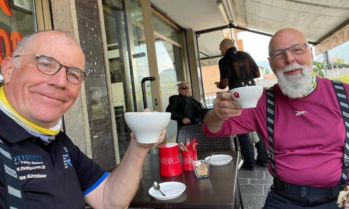 Zwei Motorradfahrer mit Kaffeetassen in der Hand bei einer Pause in einem Cafe