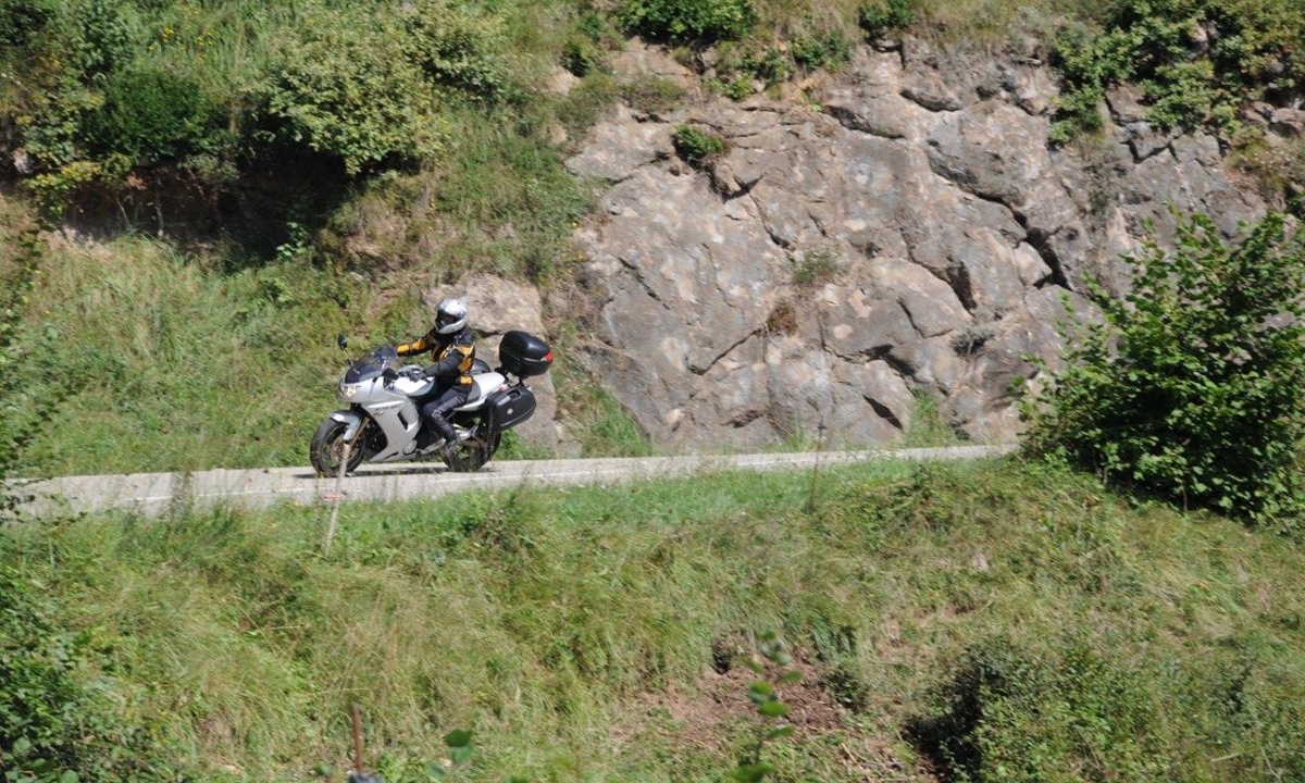 ein Motorradfahrer faehrt eine an einer Felswand entlangfuehrende Strasse entlang