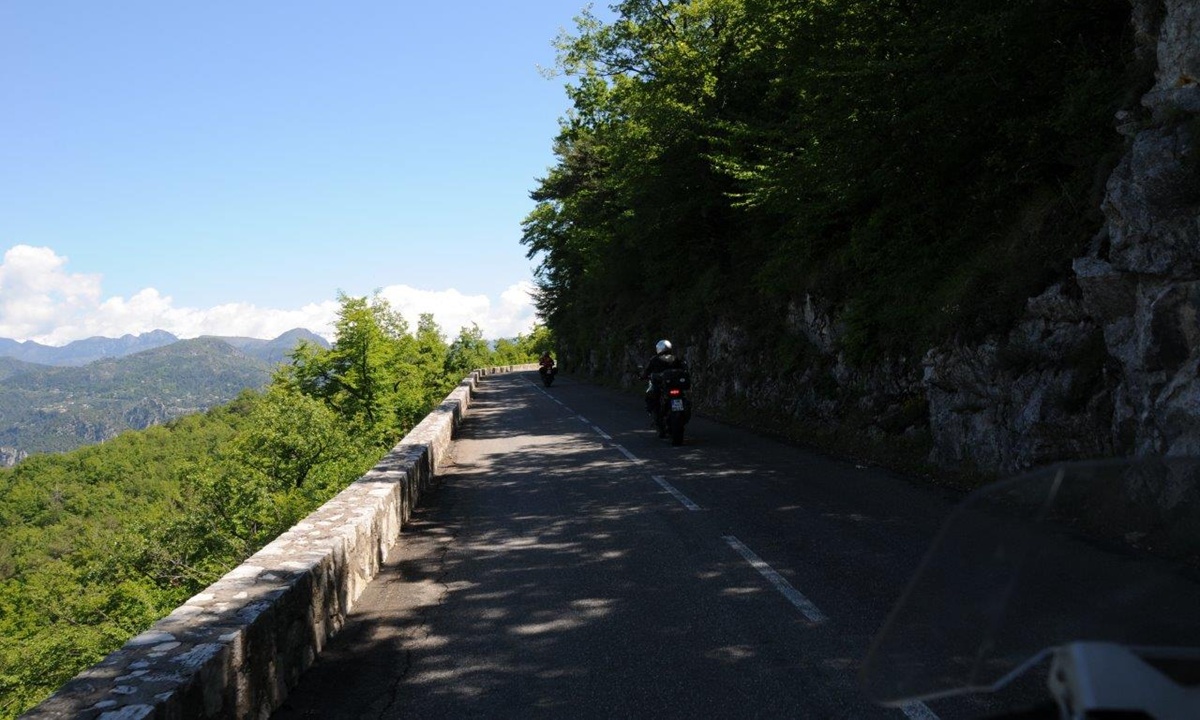 Motorradfahrer fahren hintereinander auf einer schmalen an einer Steilwand entlangfuehrenden Strasse entlang