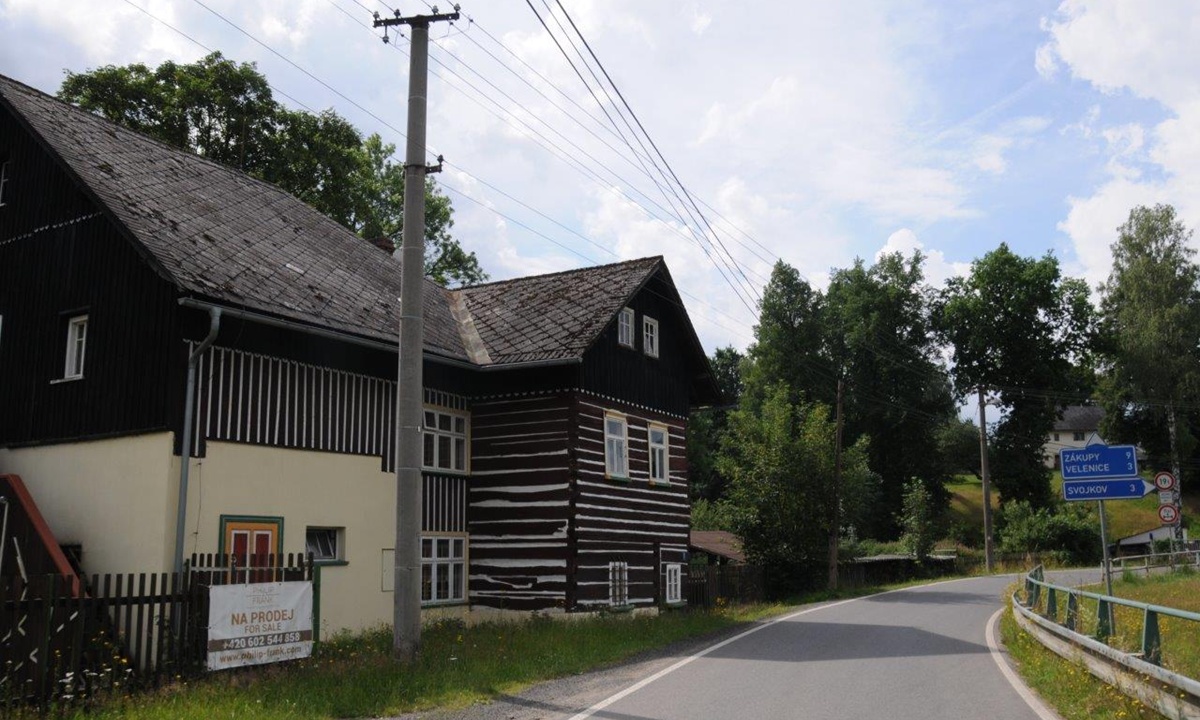 schwarz-weisses Haus mit "zu verkaufen" Schild an einem Strassenrand
