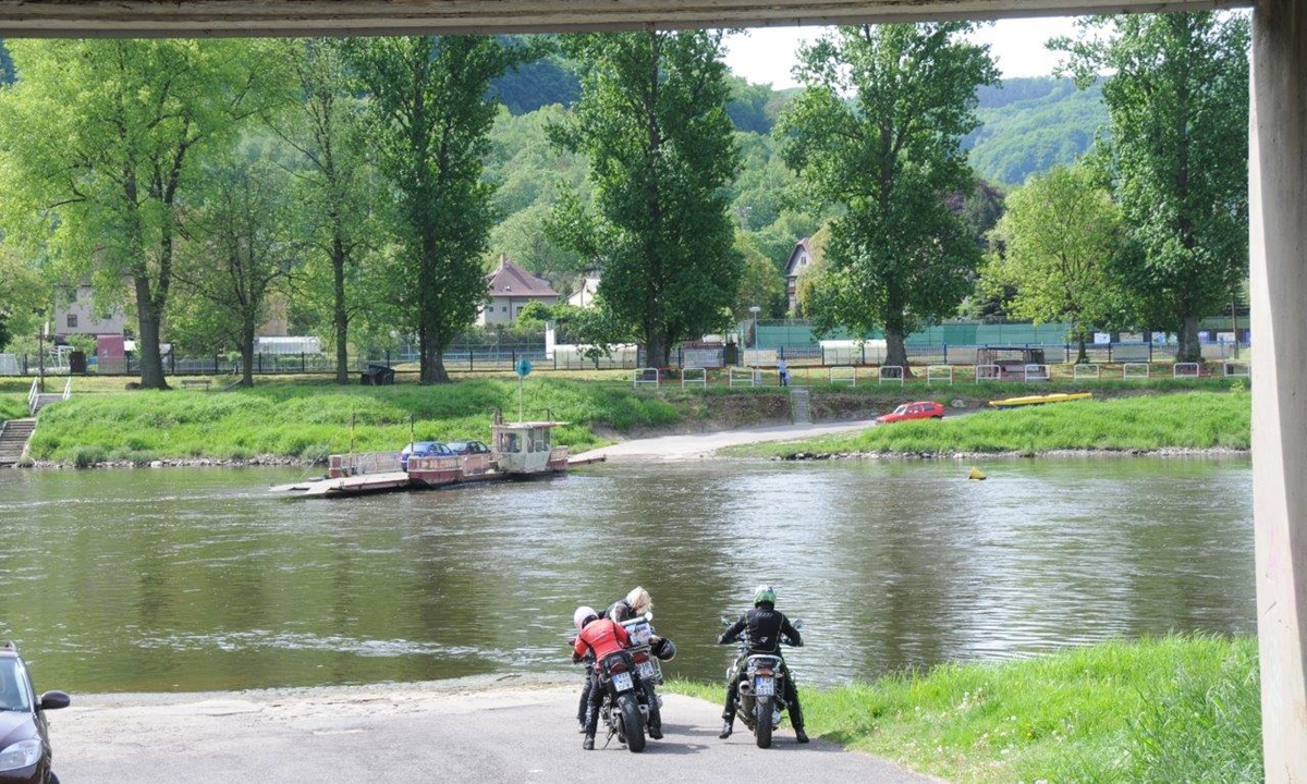 drei Motorraeder warten am Ufer eines Flusses auf eine Faehre