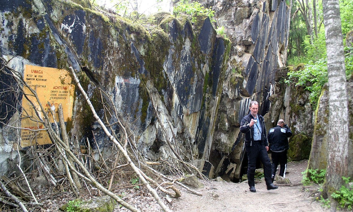 Mann in Motorradkleidung neben moosbewucherten Betonruinen