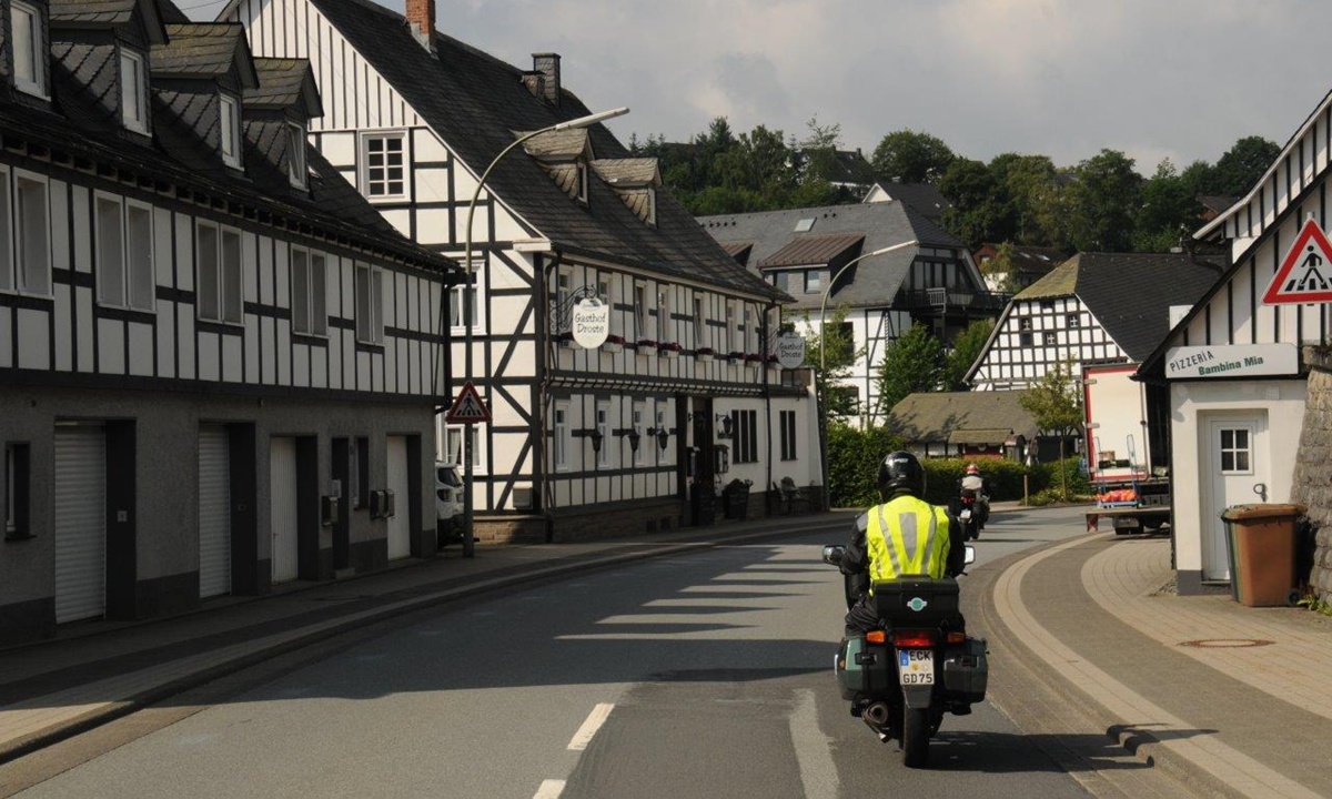 ein Motorradfahrer mit gelber Warnweste faehrt durch einen Ort mit vielen Fachwerkhaeusern