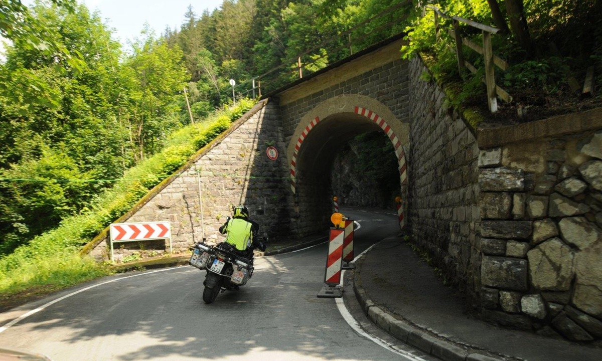 Ein Motorrad faehrt auf einen schmalen Tunnel unterhalb einer Eisenbahnstrecke zu