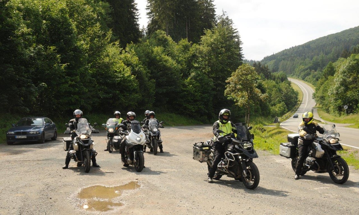 Eine Gruppe Motorradfahrer steht auf einem Schotterparkplatz am Strassenrand