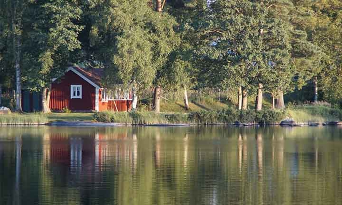 ein rotes Holzhaus mit weissen Details steht in einem Wald und spiegelt sich in einem glatten See