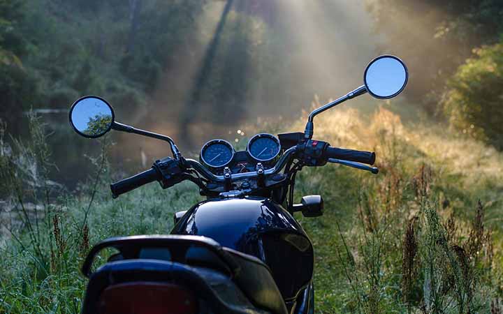 Ein schwarzes Motorrad steht auf einer Lichtung in einem Waldstueck; durch die Baeume fallen goldene Lichtstrahlen auf die Lichtung