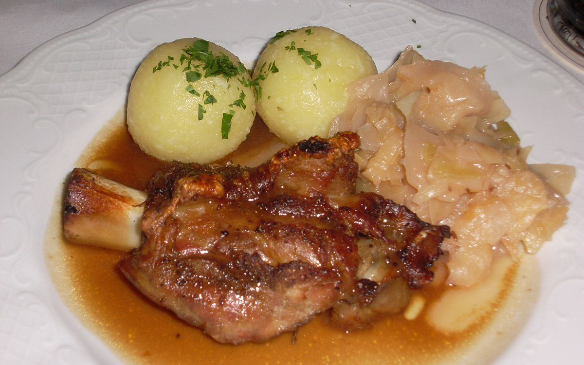 weisser Teller mit einer Schweishaxe, zwei Kloessen und Salat darauf bei unserer "Die Sau ist tot"-Motorradreise