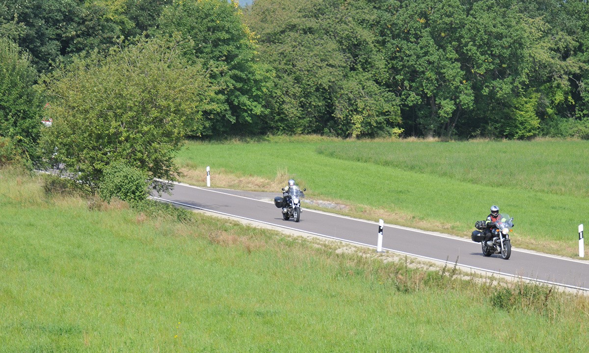 zwei Motorraeder fahren auf einer Landstrasse ueber eine gruene Wiese
