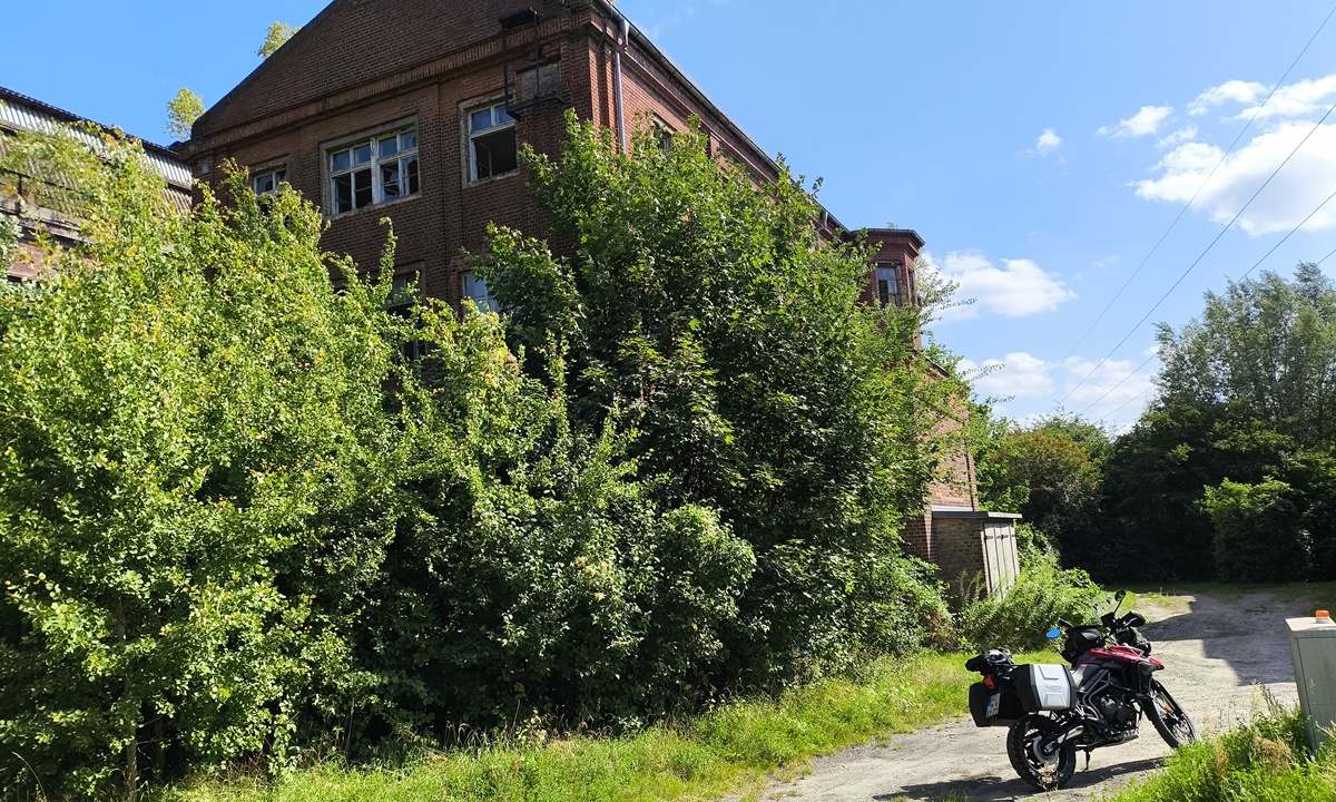 ein Motorrad parkt in einer gruenen Ladschaft, im Hintergrund befindet sich die Ruine eines Gebaeudes