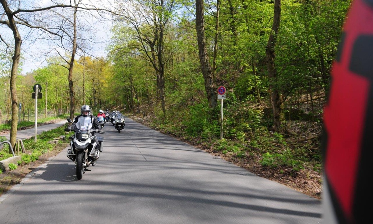 Motorraeder fahren hintereinander auf einem bewaldeten Stueck einer Landstrasse