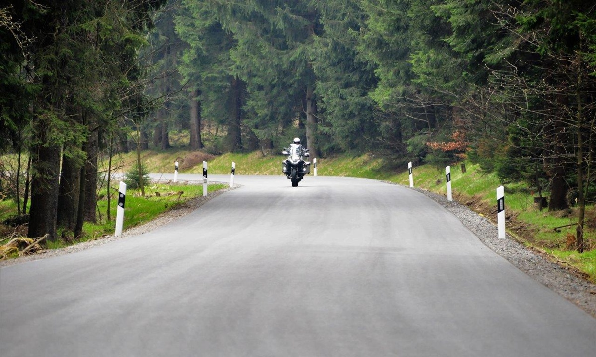 Motorrad auf einer breiten nagelneuen Teerstrasse in einem Waldstueck
