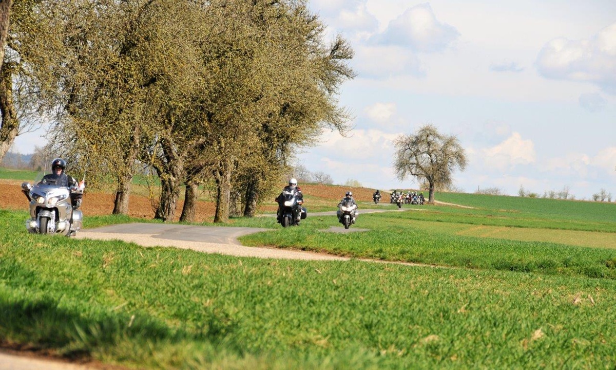 mehrere Motorraeder auf einer schmalen kurvigen Strasse zwsichen gruenen Feldern