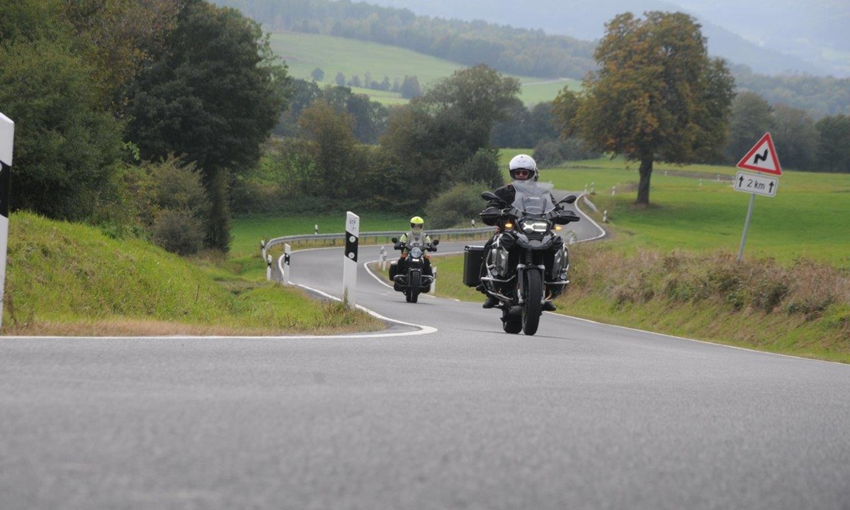 zwei Motorraeder fahren auf einer kurvigen Landstrasse ueber Felder und Wiesen