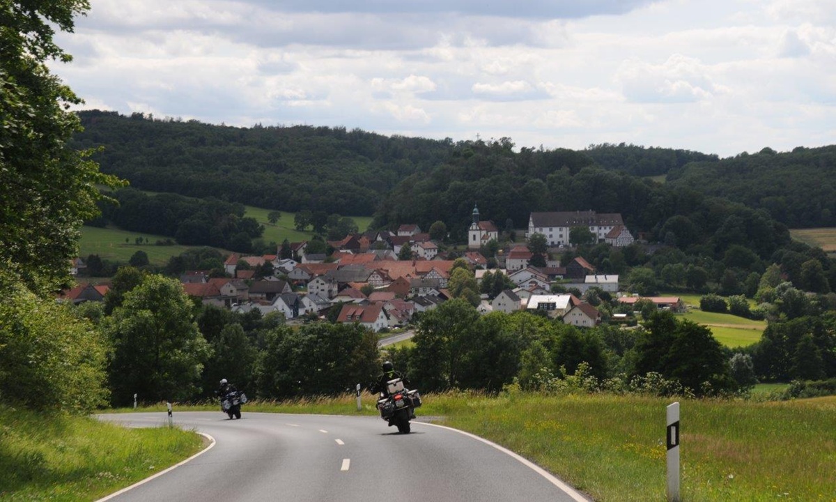 zwei Motorraeder fahren auf eine kleine Siedlung im laendlichen Raum zu