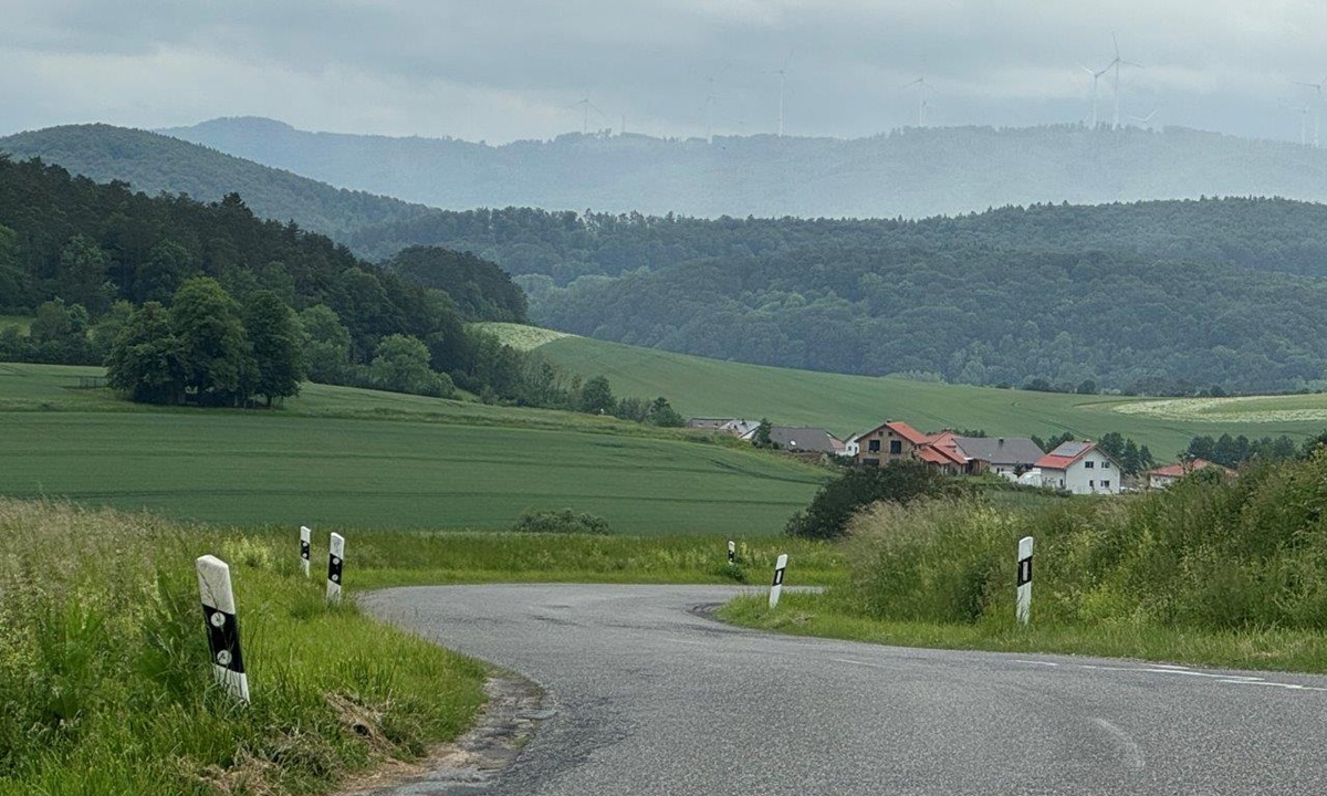 kurvige auf eine Siedlung zufuehrende Strasse in einer huegeligen Landregion