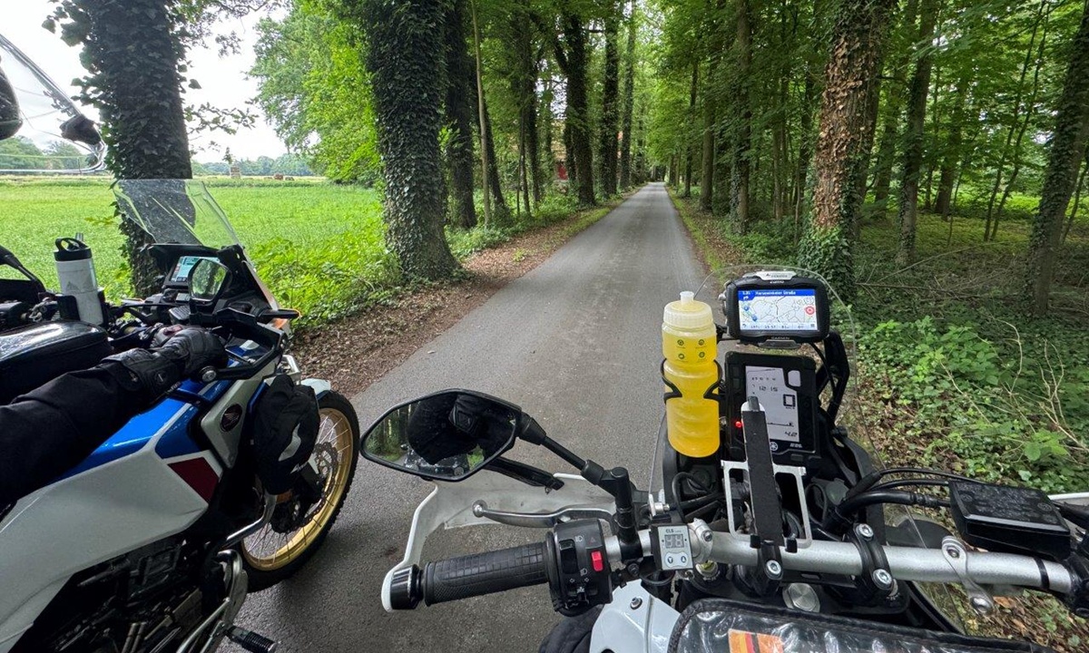 POV Aufnahme einer Motorradfahrers der neben einem weiteren Motorrad auf einer schmalen Strasse durch ein Wladstueck faehrt
