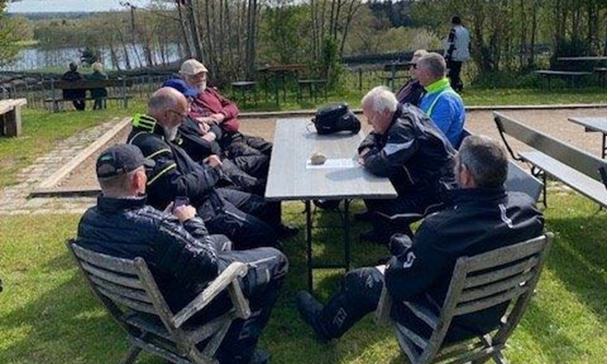 Eine Gruppe Personen in Motorradkleidung sitzt in gemuetlicher Runde um einen Tisch